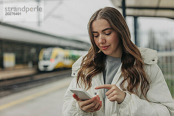 Frau benutzt Smartphone am Bahnhof