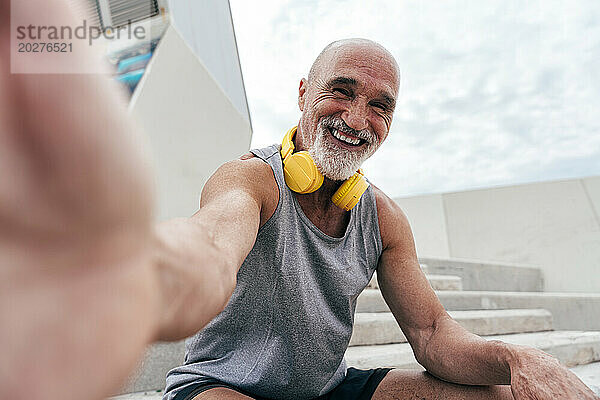 Glücklicher älterer Mann  der auf der Treppe sitzend ein Selfie macht