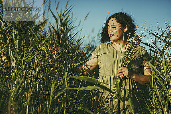 Lächelnde reife Frau  die Gras auf dem Feld berührt