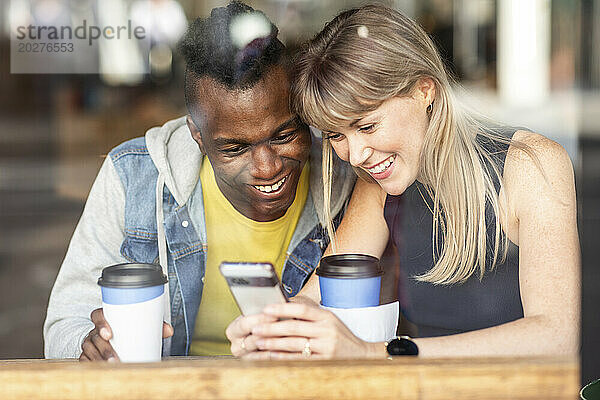 Aufgeregte Freunde  die im Café sitzen und ihr Smartphone teilen