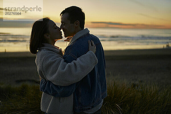 Zärtliche Freundin und Freund umarmen sich am Strand bei Sonnenuntergang