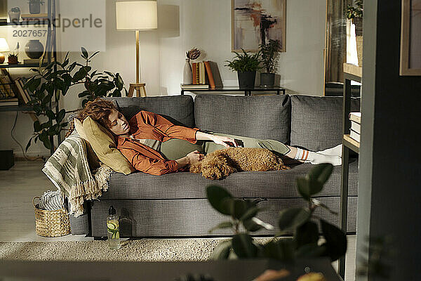 Expectant woman resting on sofa with dog in living room