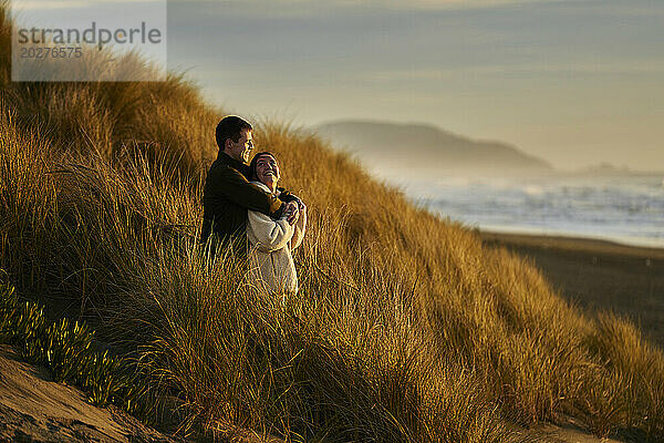 Lächelndes Paar  das sich umarmt und am Meeresstrand steht
