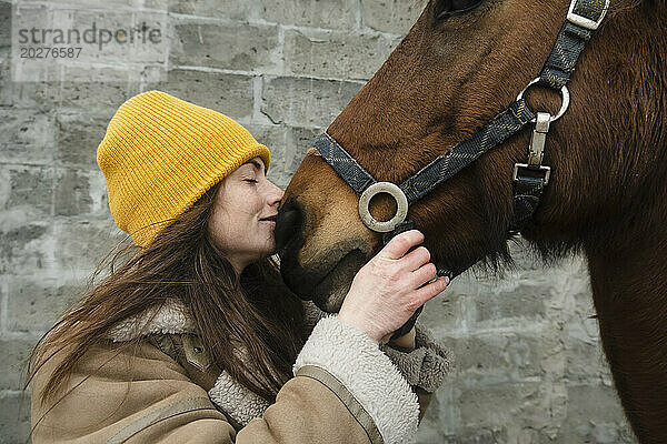 Frau küsst braunes Pferd vor der Wand
