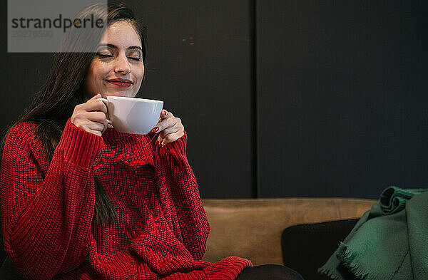 Lächelnde Frau mit geschlossenen Augen hält Kaffeetasse im Café