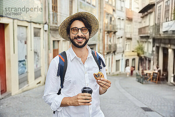 Lächelnder junger Mann mit Kaffeetasse und traditionellem Dessert Pastel de Nata