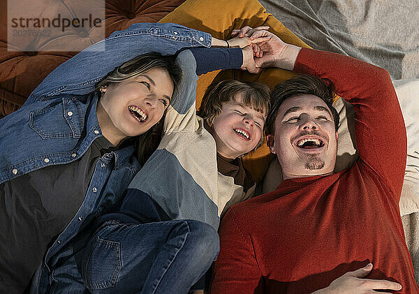 Cheerful family holding hands and enjoying on bed at home