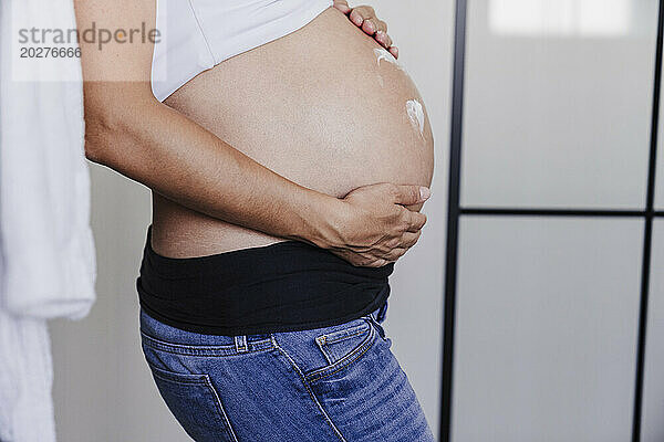 Schwangere Frau verwendet zu Hause Creme auf dem Bauch