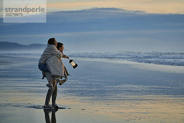 Junges Paar mit Laterne  bedeckt mit Schal  am Meeresstrand