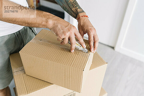 Hände eines Mannes  der im neuen Zuhause einen Karton mit einem Allzweckmesser öffnet