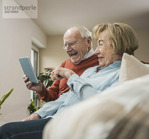 Glückliches Seniorenpaar nutzt Tablet-PC im heimischen Wohnzimmer