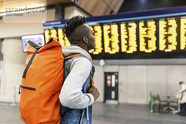Junger Rucksacktourist liest Zugfahrplan am Bahnhof