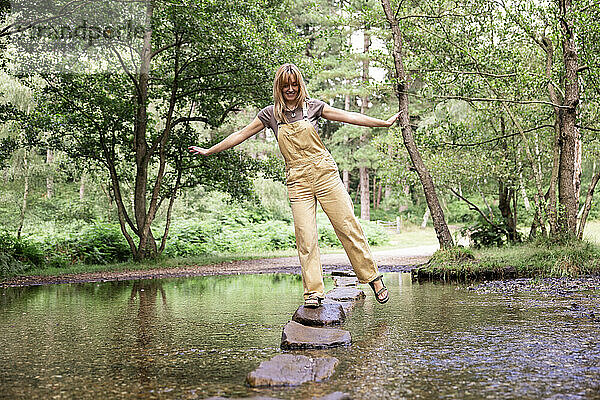 Glückliche junge Frau balanciert auf einem Felsen im Fluss