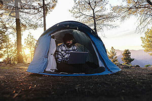 Lächelnder Freiberufler  der bei Sonnenuntergang am Laptop arbeitet