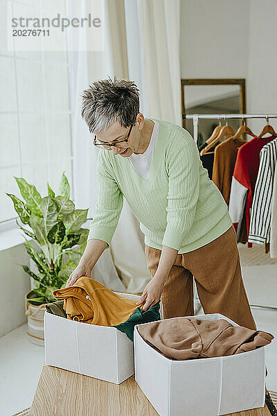 Reife Frau legt zu Hause alte Kleidung zur Spende in einen Karton