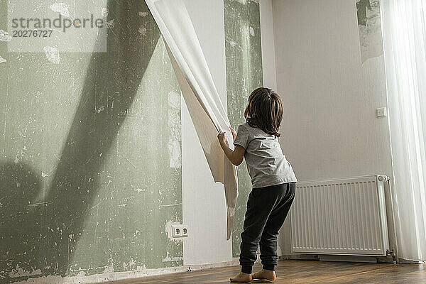 Junge schält alte Tapete von der Wand im Wohnzimmer