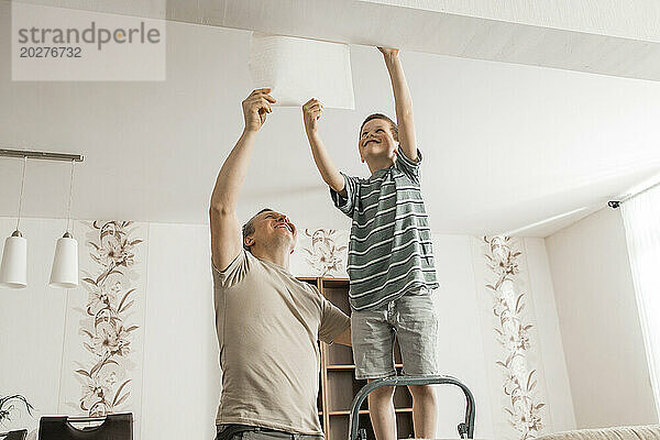 Glücklicher Junge und Vater schälen zu Hause alte Tapeten von der Decke