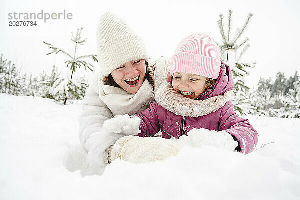 Fröhliche Mutter und Tochter amüsieren sich im Schnee im Winterpark