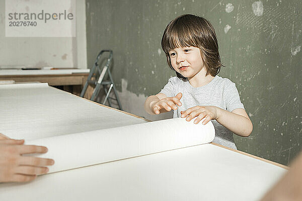 Boy rolling out wallpaper on table at home