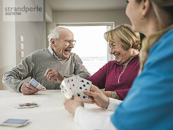 Fröhliches Paar spielt Karten mit häuslicher Pflegekraft am Tisch