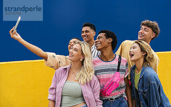Lachende multiethnische Freunde machen Smartphone-Selfies vor gelber Wand