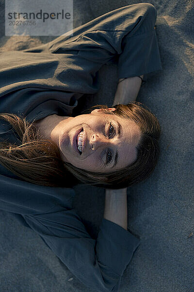 Lächelnde Frau entspannt sich im Sand am Strand
