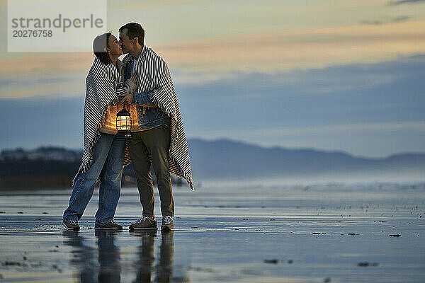 Young man with lantern kissing girlfriend at ocean beach