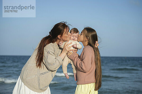 Mutter und Tochter küssen ihr kleines Mädchen am Strand