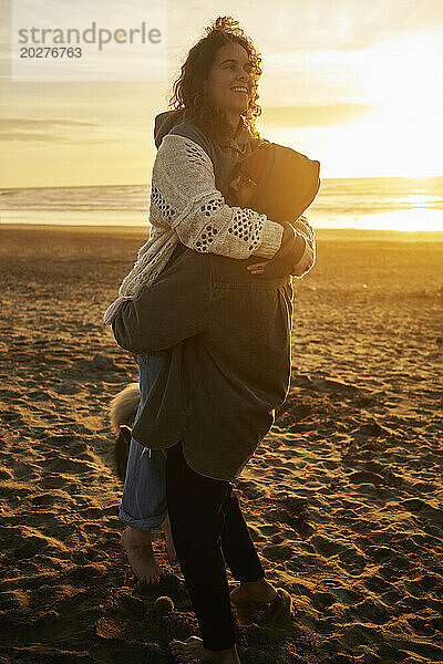 Junger Mann trägt glückliche Frau am Strand