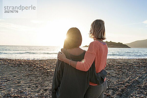 Freunde mit Armen um sich herum verbringen ihre Freizeit gemeinsam am Strand bei Sonnenuntergang