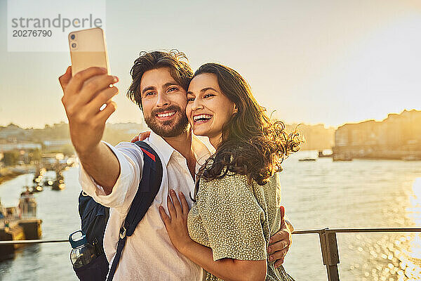 Glückliches Paar macht bei Sonnenuntergang ein Selfie mit dem Smartphone vor dem Fluss Douro