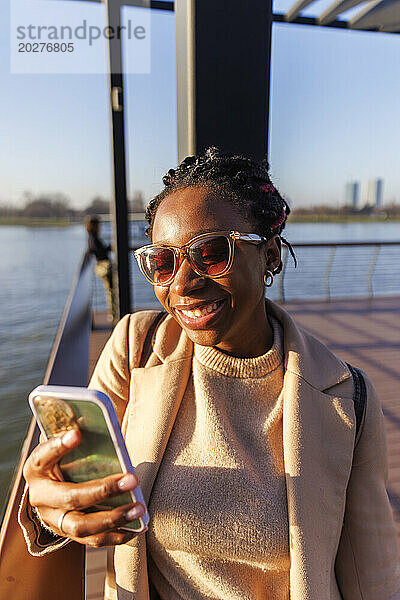 Glückliche Frau  die in der Nähe des Flusses einen Videoanruf auf ihrem Smartphone führt