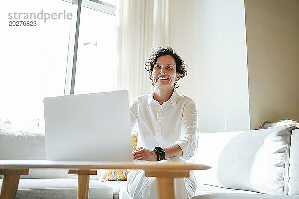 Smiling mature businesswoman with laptop sitting on sofa in lobby of hotel