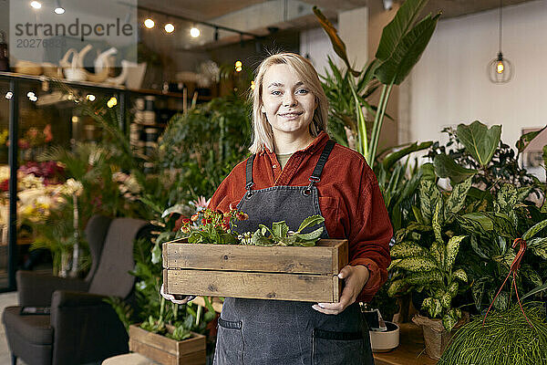 Lächelnder Gärtner hält Kiste mit Pflanzen im Gartencenter