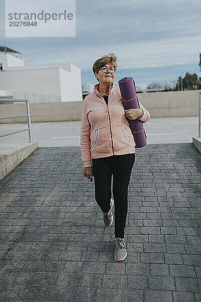 Ältere Frau mit Gymnastikmatte läuft auf Gehweg
