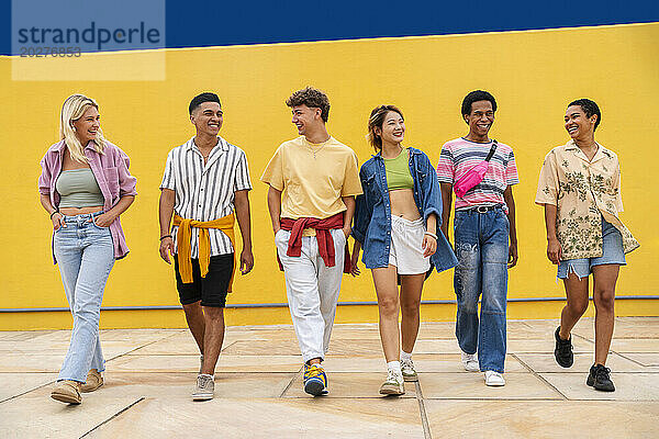 Multi-ethnic group of young friends walking side by seide in front of yellow wall