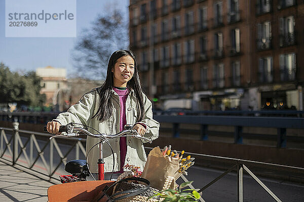 Lächelnde junge Frau läuft mit Lastenfahrrad durch die Stadt