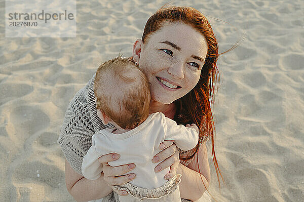 Lächelnde Frau mit kleinem Mädchen sitzt im Sand am Strand