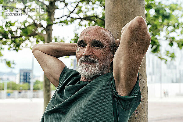 Älterer Rentner entspannt sich auf einem Baumstamm  die Hände hinter dem Kopf