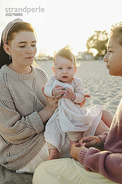 Mutter sitzt mit Kindern am Strand