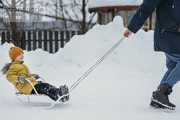 Glücklicher Sohn genießt Schlittenfahrt mit Vater im Winter im Schnee