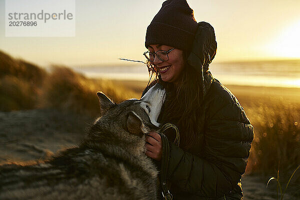 Lächelnde Frau streichelt Husky-Hund am Strand