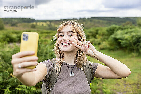 Glückliche blonde Frau  die im Wald ein Selfie mit ihrem Smartphone macht