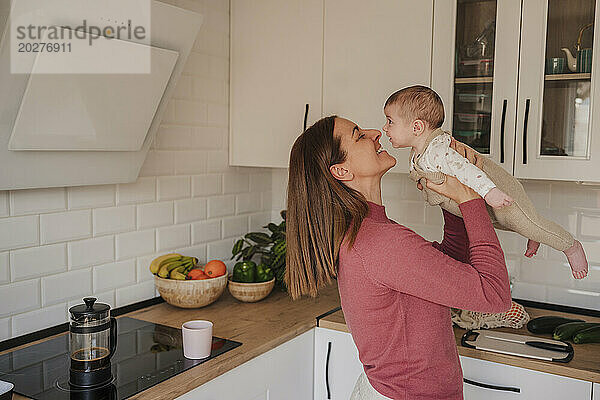 Smiling mother embracing and playing with baby daughter in kitchen