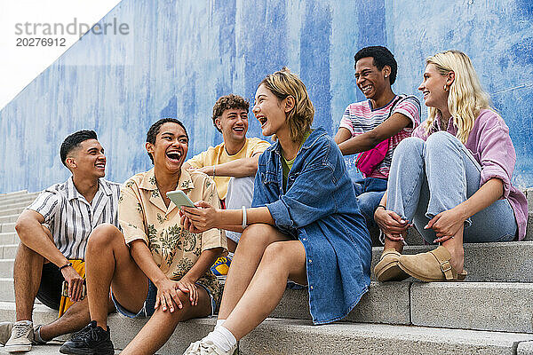 Fröhliche Gruppe junger Leute  die auf Stufen vor der Wand lachen