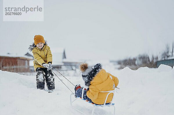 Boy pulling brother on sled in winter