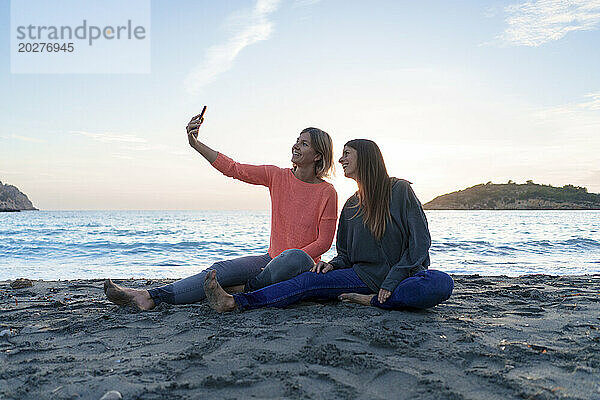 Fröhliche Freunde machen gemeinsam ein Selfie am Strand bei Sonnenuntergang