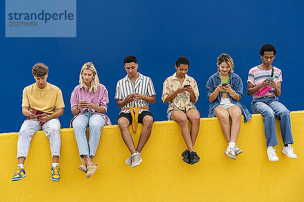 Fröhliche Freunde in bunter Kleidung sitzen auf Gelb und nutzen ihre Smartphones