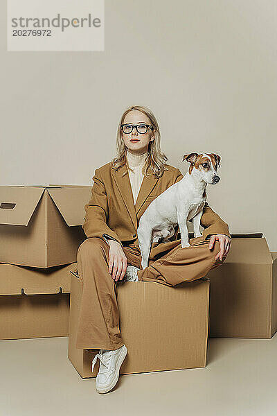 Geschäftsfrau sitzt mit Hund auf Karton vor weißem Hintergrund