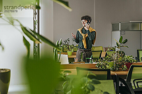 Businessman talking on smart phone near plants in office